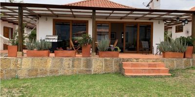 Espectacular Casa Campestre a pocos minutos del casco urbano de Villa de Leyva, amoblada y dotada con electrodomésticos, decoración y utensilios. Construida en un lote de 1.550 metros cuadrados, tiene 3 modulos, con un area interior de 180 metros cuadrados, mas 160 metros cuadrados de terrazas y áreas cubiertas. En el primer módulo tiene la habitación principal, con baño privado, y vestier, este primer módulo está separado de la zona social por una terraza cubierta, en el segundo módulo está la zona social, compuesta de sala con chimenea, comedor, cocina abierta, con zona de lavandería, baño social y terraza. Separado por otra terraza cubierta, está el tercer módulo, el cual tiene dos habitaciones, cada una con cama doble y dos camas sencillas, baño privado y terraza cubierta. Tiene una zona de parqueo para 4 carros, más un parqueadero cubierto para un quinto vehículo. Toda la casa está rodeada de terrazas cubiertas y jardines. 
