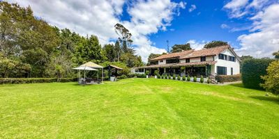 Casa principal de 480 M2 en 2 plantas, con 5 habitaciones, 5 baños, a tan solo 8 minutos del pueblo, en un terreno de 3,13 fanegadas, amplia zona social con estudio con chimenea, salón comedor, gran salón de juegos y un cuarto de televisión, rodeada de hermosos jardines y linda arborización. Casa completamente equipada, perfectamente apta para vivir en el campo cómodamente, rodeado de naturaleza, paz y tranquilidad, ubicada en una zona muy segura con varias casas de familia. Cómoda casa de mayordomos con 2 habitaciones y salón comedor. Actualmente el uso del suelo es "parcelación campestre", con un altísimo potencial de valorización en el corto plazo, teniendo en cuenta la próxima construcción de la perimetral de oriente que conectará los llanos Orientales con el norte de Bogotá. Se recibe permuta, hasta por 30% del valor por inmuebles en Bogotá o USA.