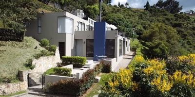 Linda casa de 315 m2 + 130 m2 de terrazas. Dos pisos. Sala con chimenea de leña, comedor, cocina abierta gas propano, alacena, baño social, dos depósitos, zona de lavandería, cuarto y baño de servicio. y otra área de 25 mts2 cubierta. Family room, tres alcobas cada una con baño y la alcoba principal con walking closet y chimenea, oficina y tres terrazas. Mas casa de huéspedes o cuidanderos. Tiene un tanque subterráneo de 8 m3, 3 pozos sépticos, Zona de acceso y parqueo de 240 mt2. Todo el perímetro del lote está cercado con alambre de púas y cerco eléctrico. Tanque de agua de 5.000Lt. Carpintería Italiana a prueba de incendio. Escaleras y superficies en madera Teca natural. Cocina Brasilera marca Favorita. Cortinas (Screen) eléctricas. Pisos de madera alemanes. Sendero ecológico que lleva a un mirador. Zona de bosque nativo (Reserva natural). Acceso vía pavimentada y cerca a centro comercial.